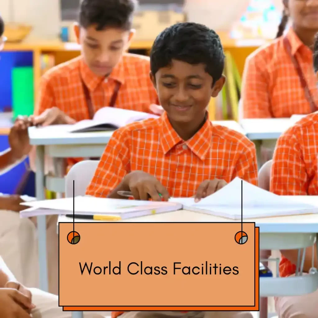 A classroom scene with children in orange-checkered school uniforms sitting at desks and smiling while studying. A label in the foreground reads ‘World Class Facilities.