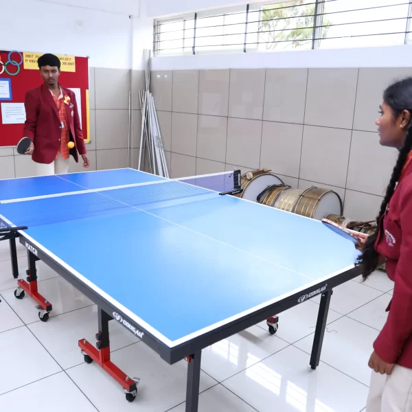 Two students playing table tennis in an indoor room.