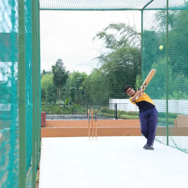 A person practicing cricket batting inside a netted practice area.