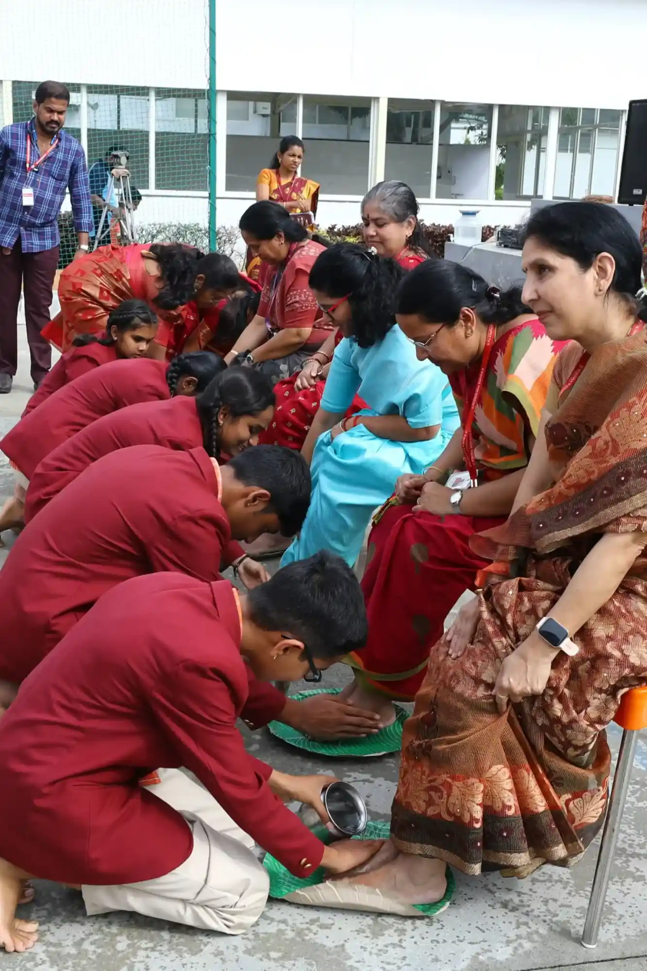 Students in maroon uniforms honoring teachers with a traditional feet-washing ceremony.