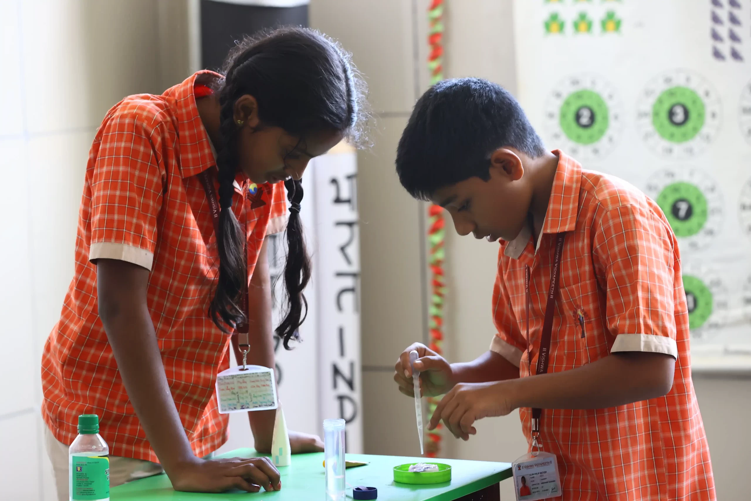 Two students in orange checkered uniforms are engaged in a science experiment, working with laboratory equipment at a table.