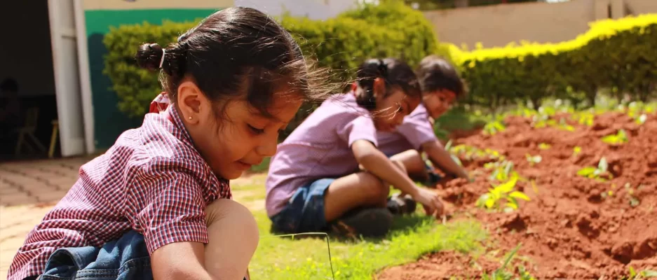 Young children in school uniforms planting saplings in a garden as part of an outdoor activity at Vishwa Vidyapeeth School.