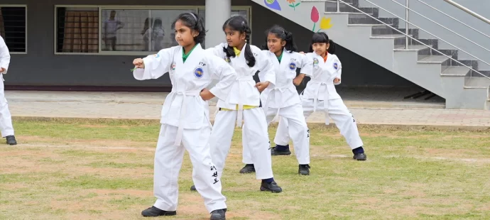 Young girls in martial arts uniforms practice in an outdoor area, performing synchronized movements.