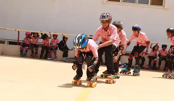 Children in protective gear learning to roller skate outdoors, guided by an instructor at Vishwa Vidyapeeth School.