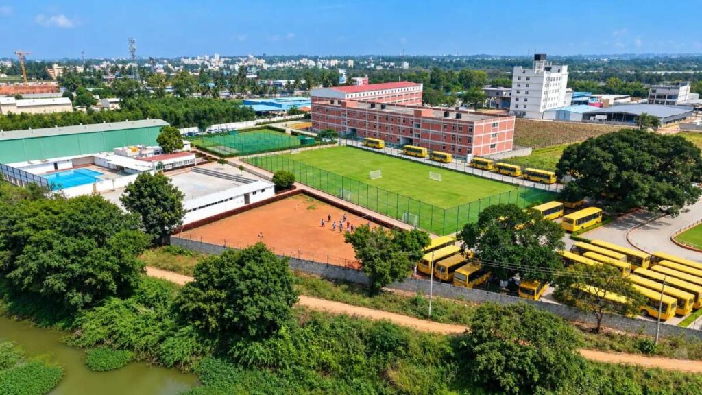 Aerial view of a lush green school campus featuring spacious playgrounds, sports facilities, academic buildings, and landscaped surroundings.