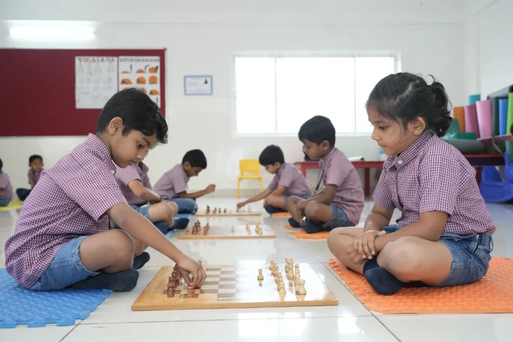 School students in uniform sitting cross-legged on classroom mats, participating in an interactive educational activity with learning materials.